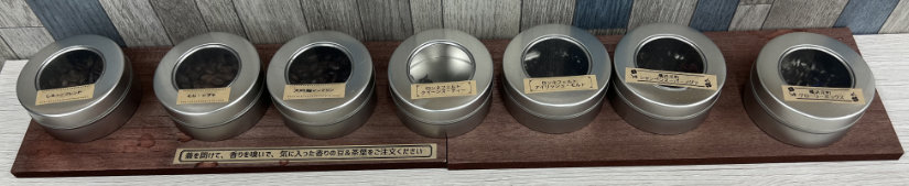 Coffee beans and tea leaves samples in metal cans with clear lids.