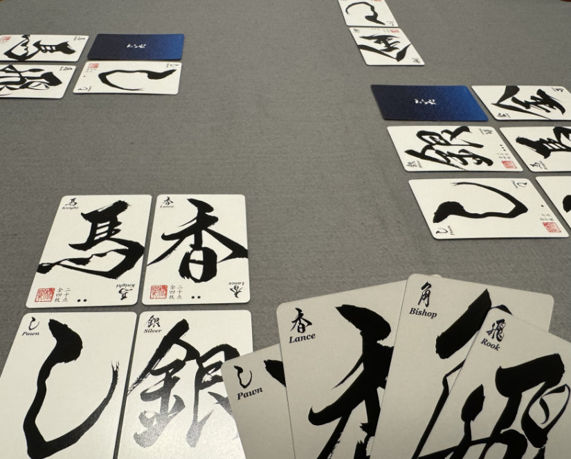 Angled view of the play space, cards sitting on grey felt. Four cards being held in the hand are in the foreground.