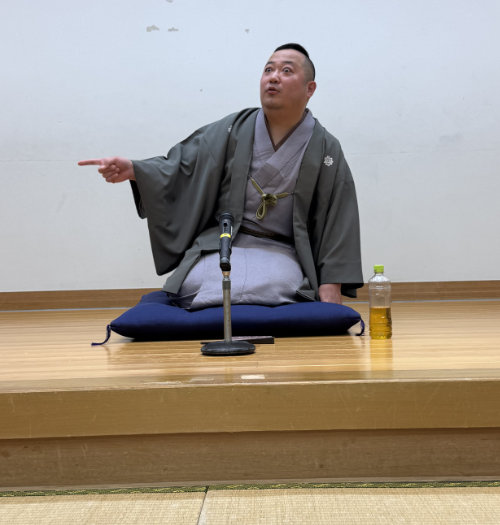 Rakuten performing rakugo, acting surprised and pointing.