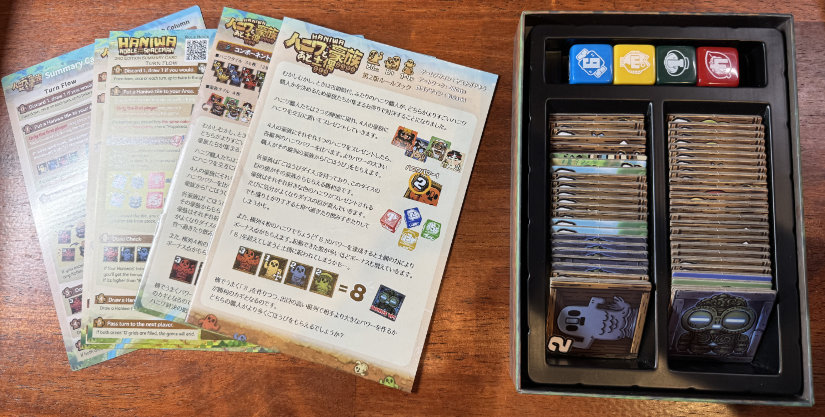 Box components. Tiles and dice are in the box, with rulebooks spread out on the desk.