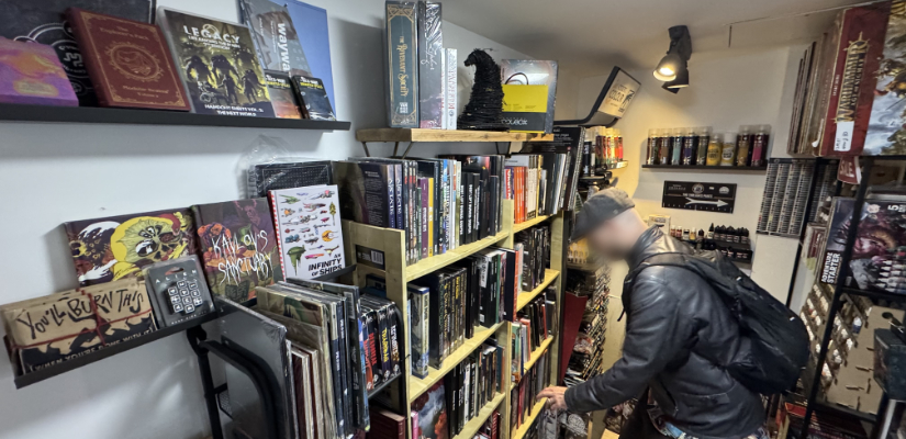 The author in a leather jacket perusing shelves of RPGs. Paints are in the background.