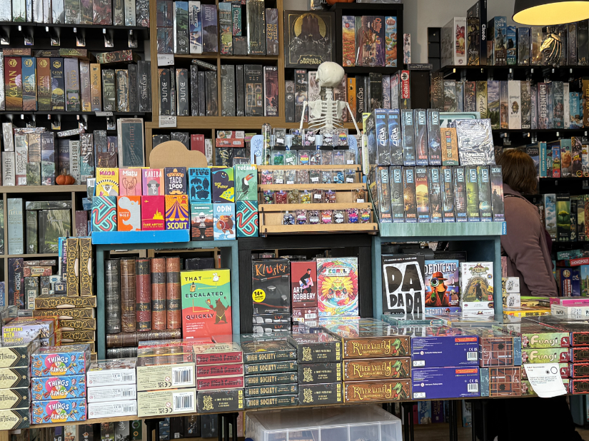 Lots of card and board games neatly arranged. A table in the foreground with many smaller boxes. Wall shelves in the back with larger boxed games.