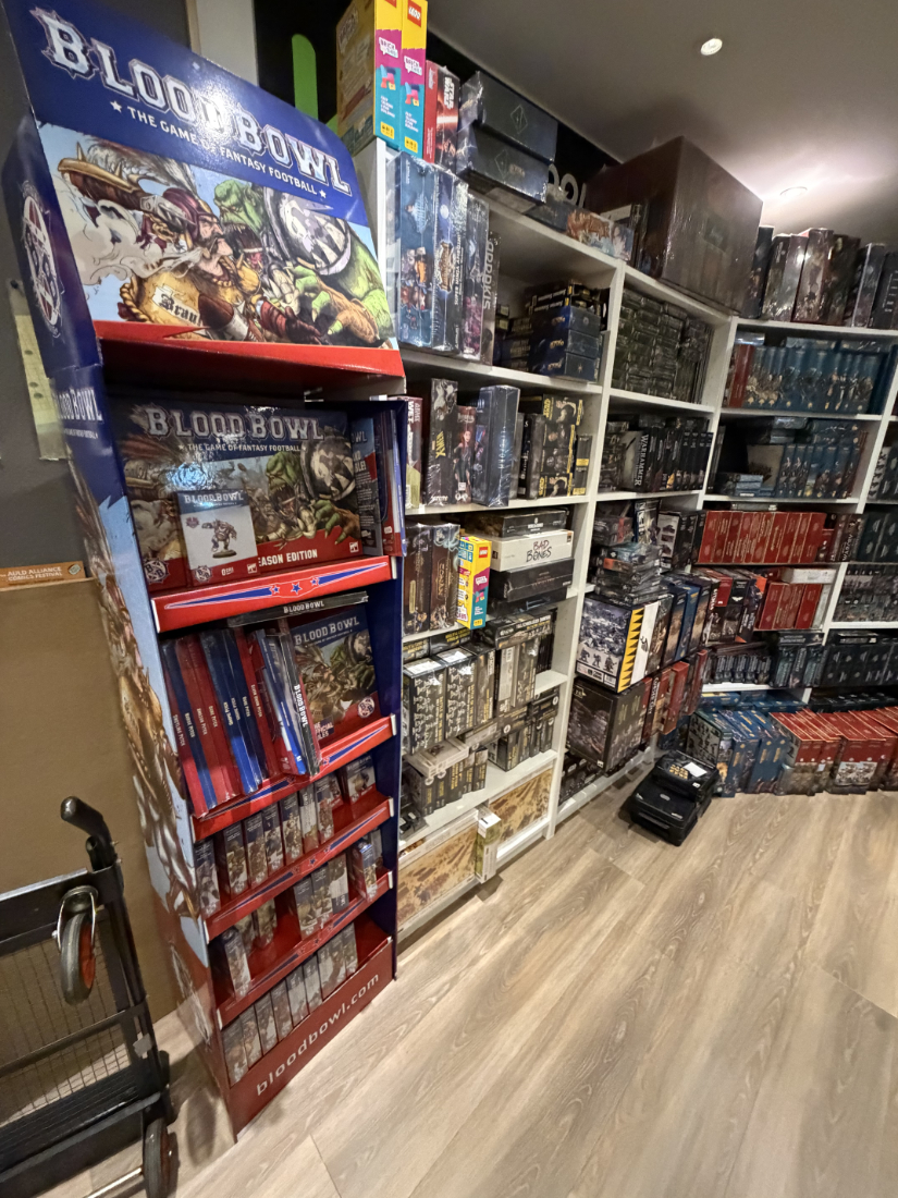 Blood Bowl and an assortment of miniature game boxes packed shelves.
